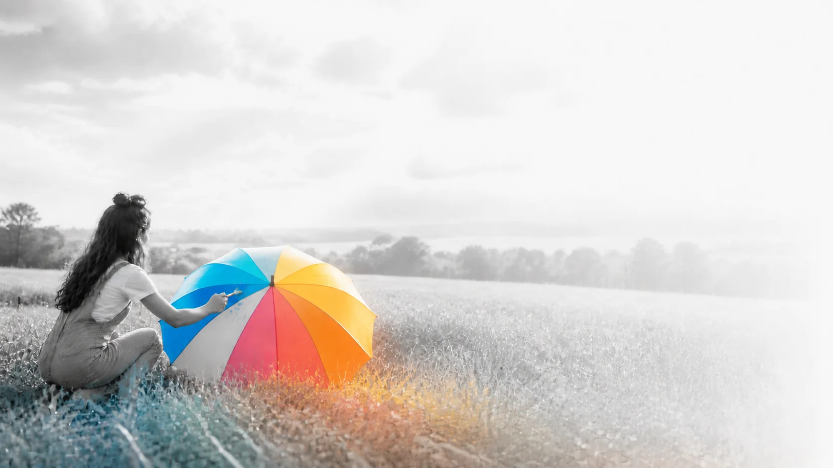 A woman in a monochrome meadow painting a brightly coloured umbrella